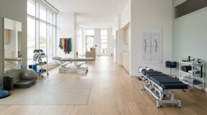 Modern rehabilitation clinic featuring separate physiotherapy and chiropractic treatment areas with professional equipment, clean interiors, and therapeutic spaces designed for neck pain assessment and rehabilitation, without people.